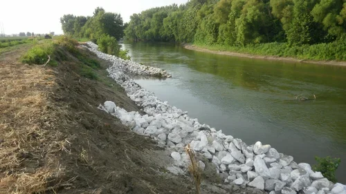 Rocks piled along the bank of a river with trees in the background.