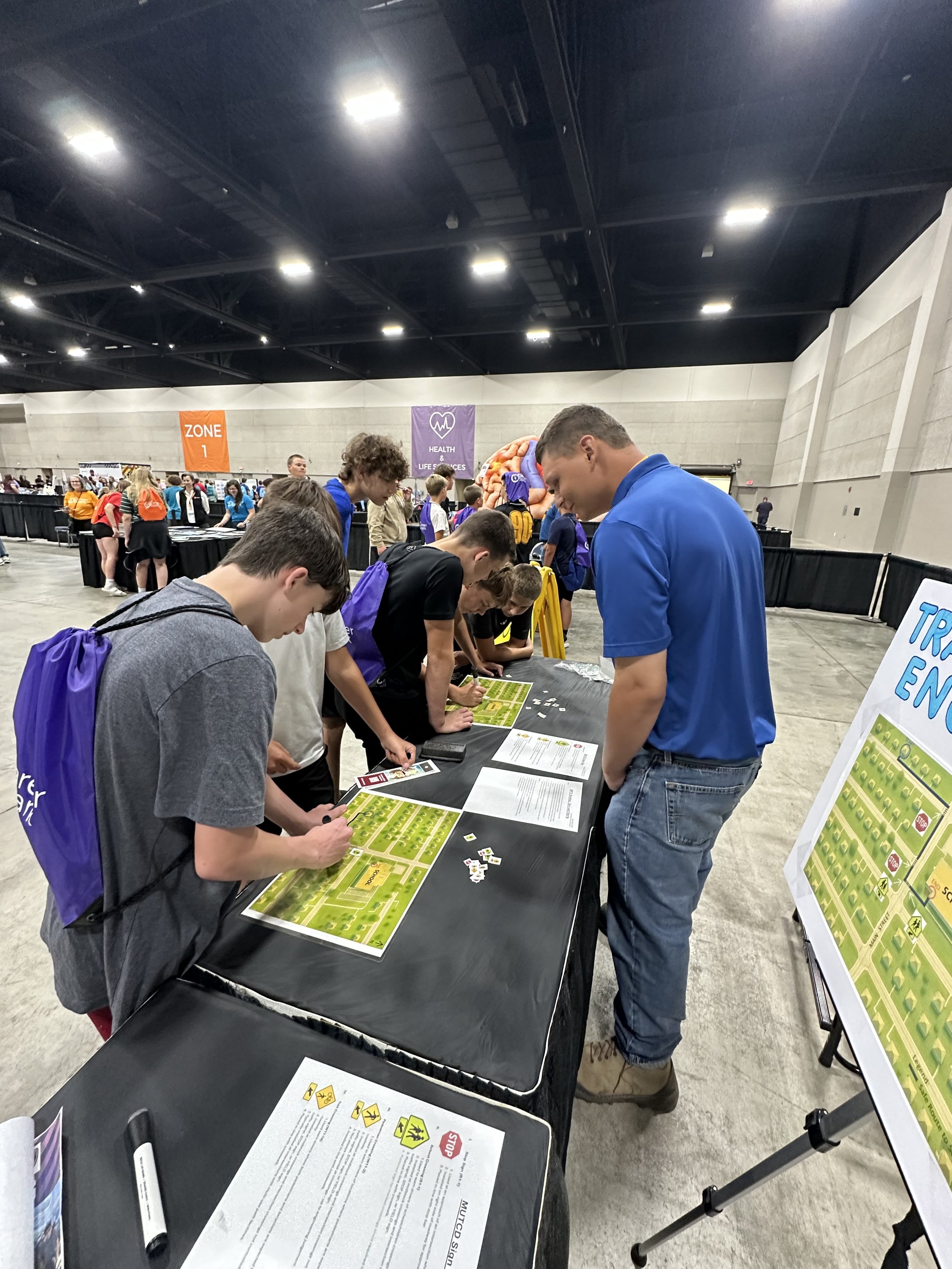 Young people playing educational games at a booth in a large indoor convention or expo center.