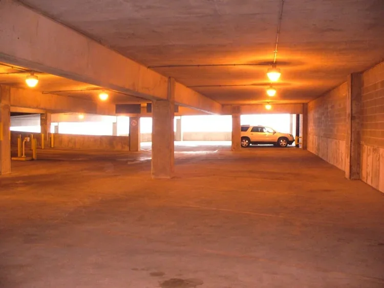 Interior view of a multi-level parking garage with a single parked silver car near the exit, illuminated by ceiling lights.