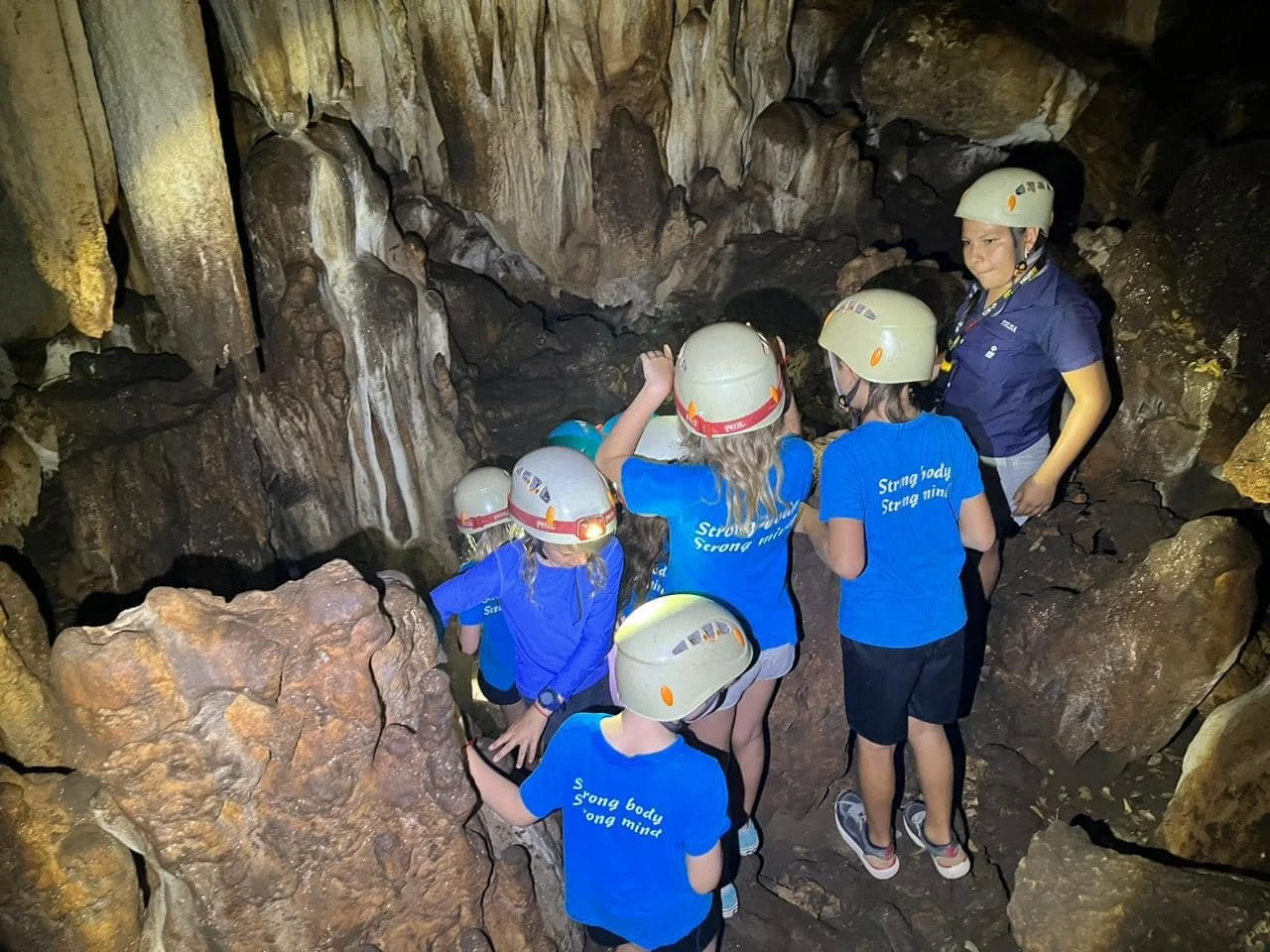 A group of children and an adult in helmets exploring a cave with rocky walls during a school field trip in Costa Rica