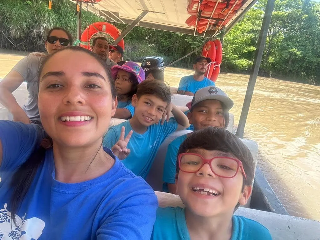 Group of kindergarten students and teachers enjoying a boat ride on a river, with green trees and life preservers in the background on a school field trip in Nosara Costa Rica