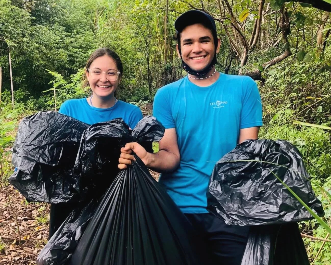 Two high school students in blue Del Mar Academy shirts holding trash bags during a cleanup event in Nosara Costa Rica's beaches