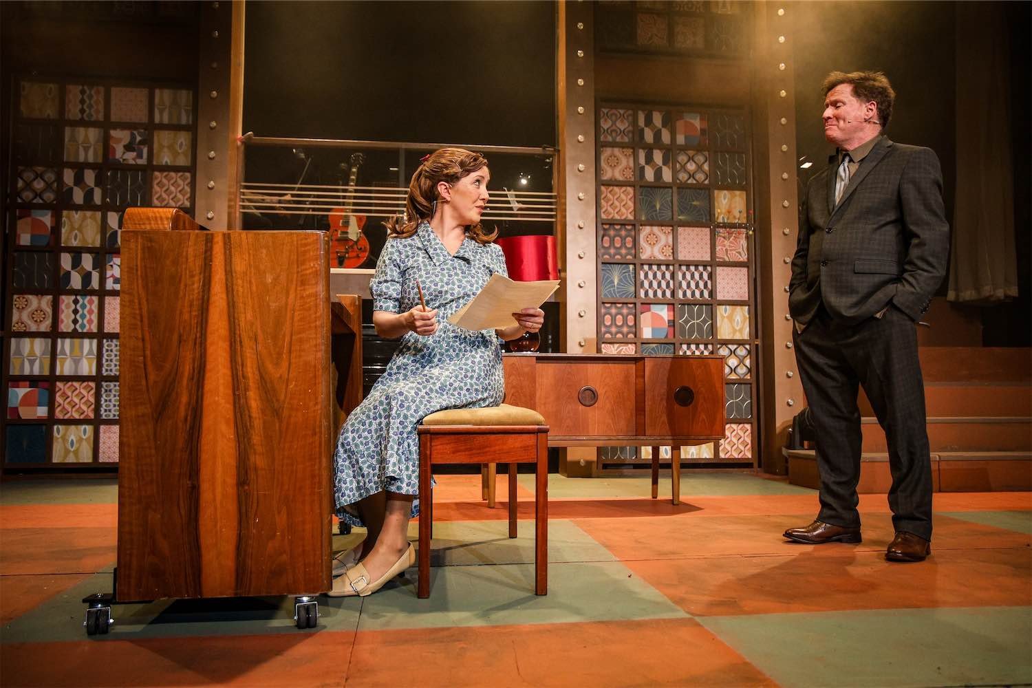 Actor Ian Prosser on stage in a performance of Beautiful with a female actress seated at a piano