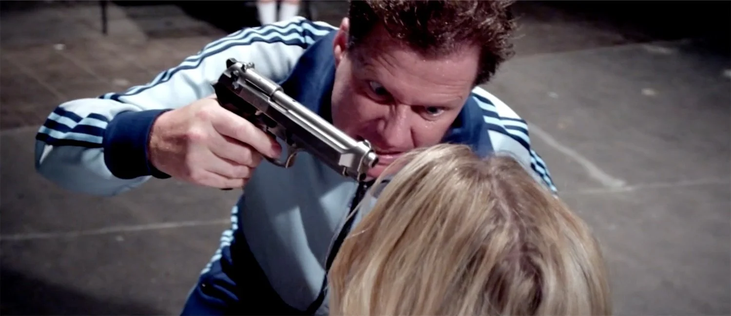 Actor Ian Prosser in character holding a gun to a woman's head in a tense confrontation.