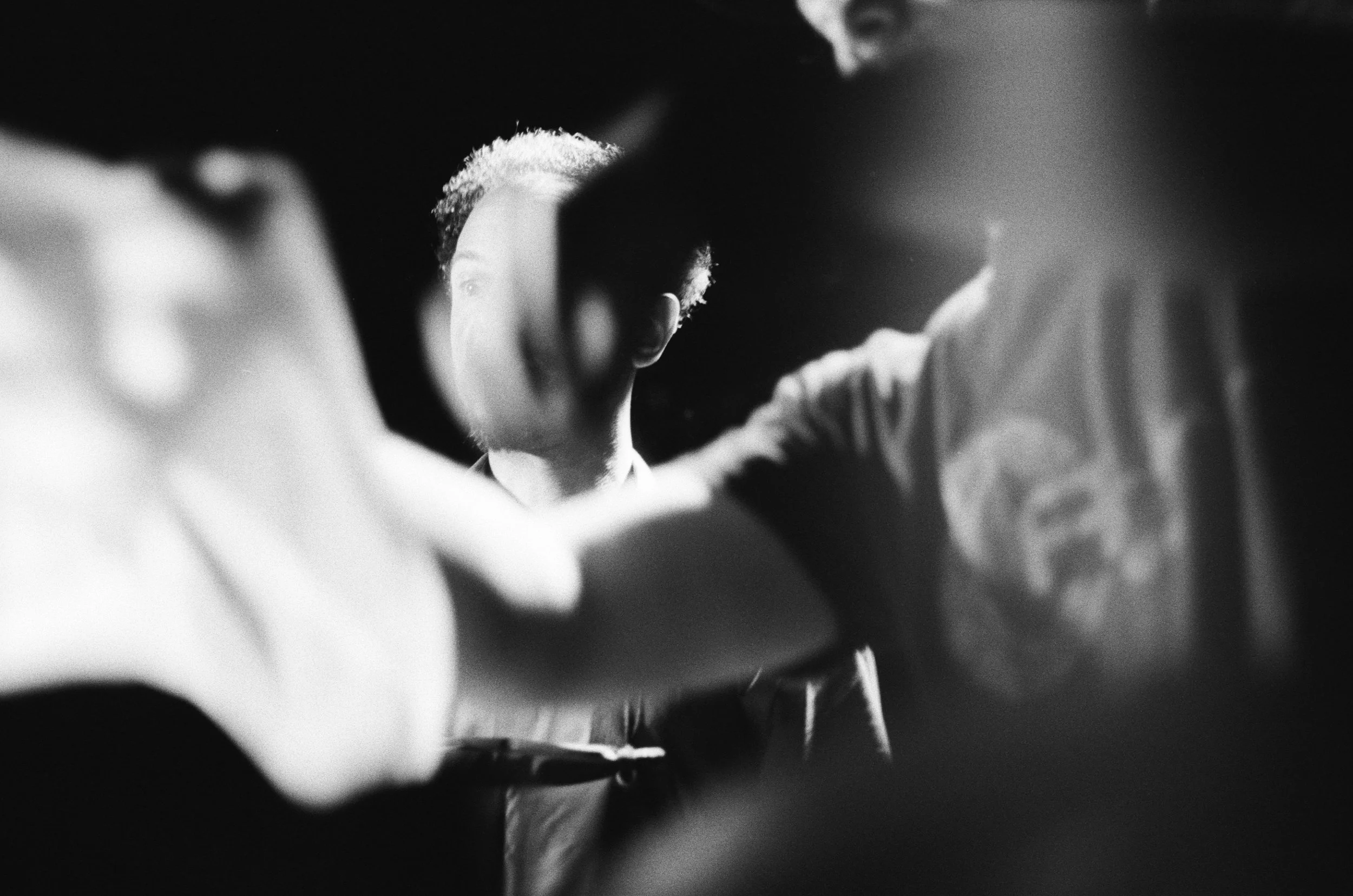 Black and white photo of a person with short hair seen through a narrow opening, creating a framing effect with blurred edges in the foreground.