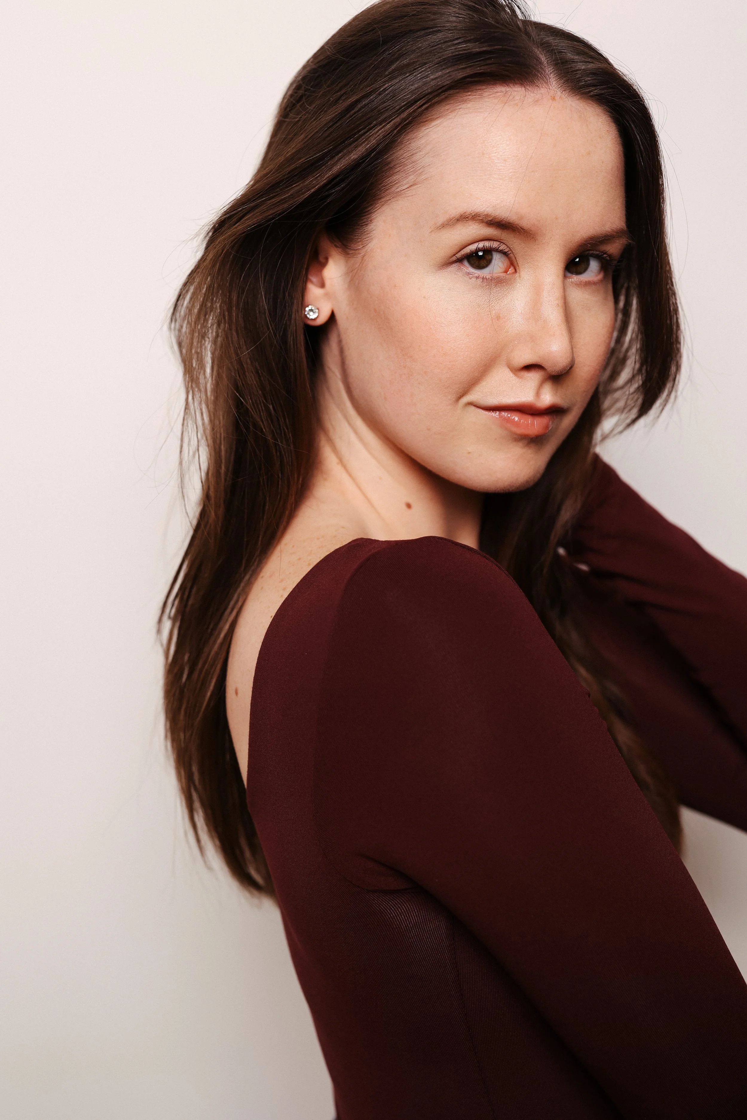 A woman with brown hair and earrings, wearing a maroon top, looking at the camera with a slight smile.