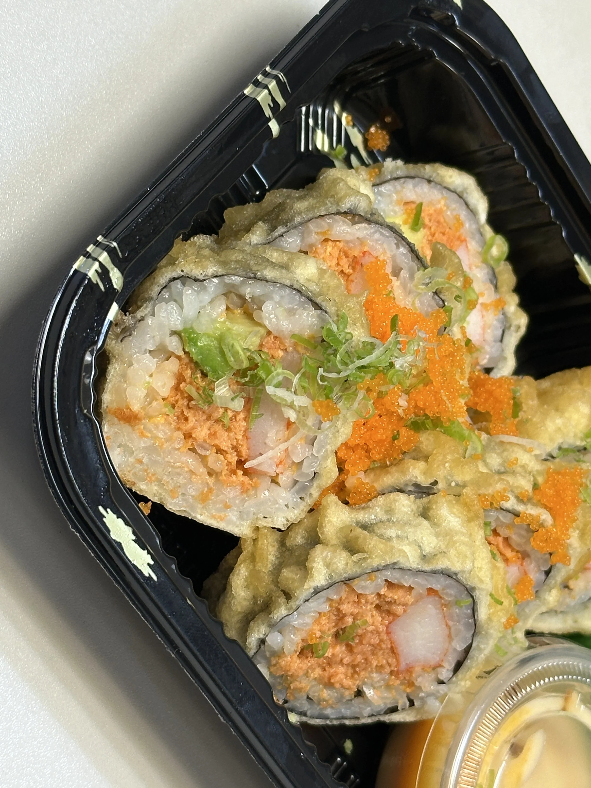 A black plastic takeout container filled with assorted sushi rolls, topped with green onions and orange fish roe.