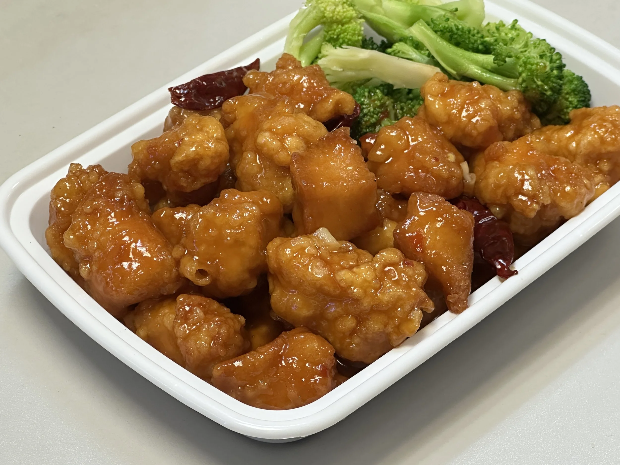 Close-up of a white dish filled with orange glazed chicken chunks and green broccoli.