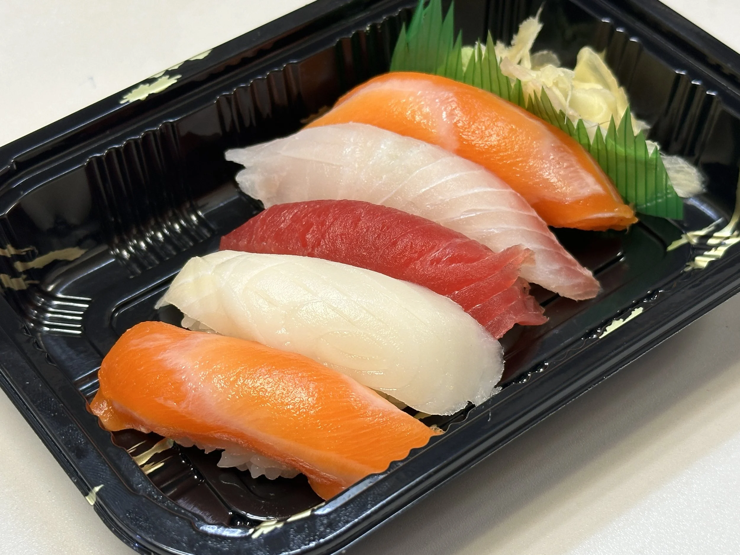 Assorted slices of fresh sashimi including salmon, tuna, white fish, and yellowtail in a black plastic tray with garnishes.