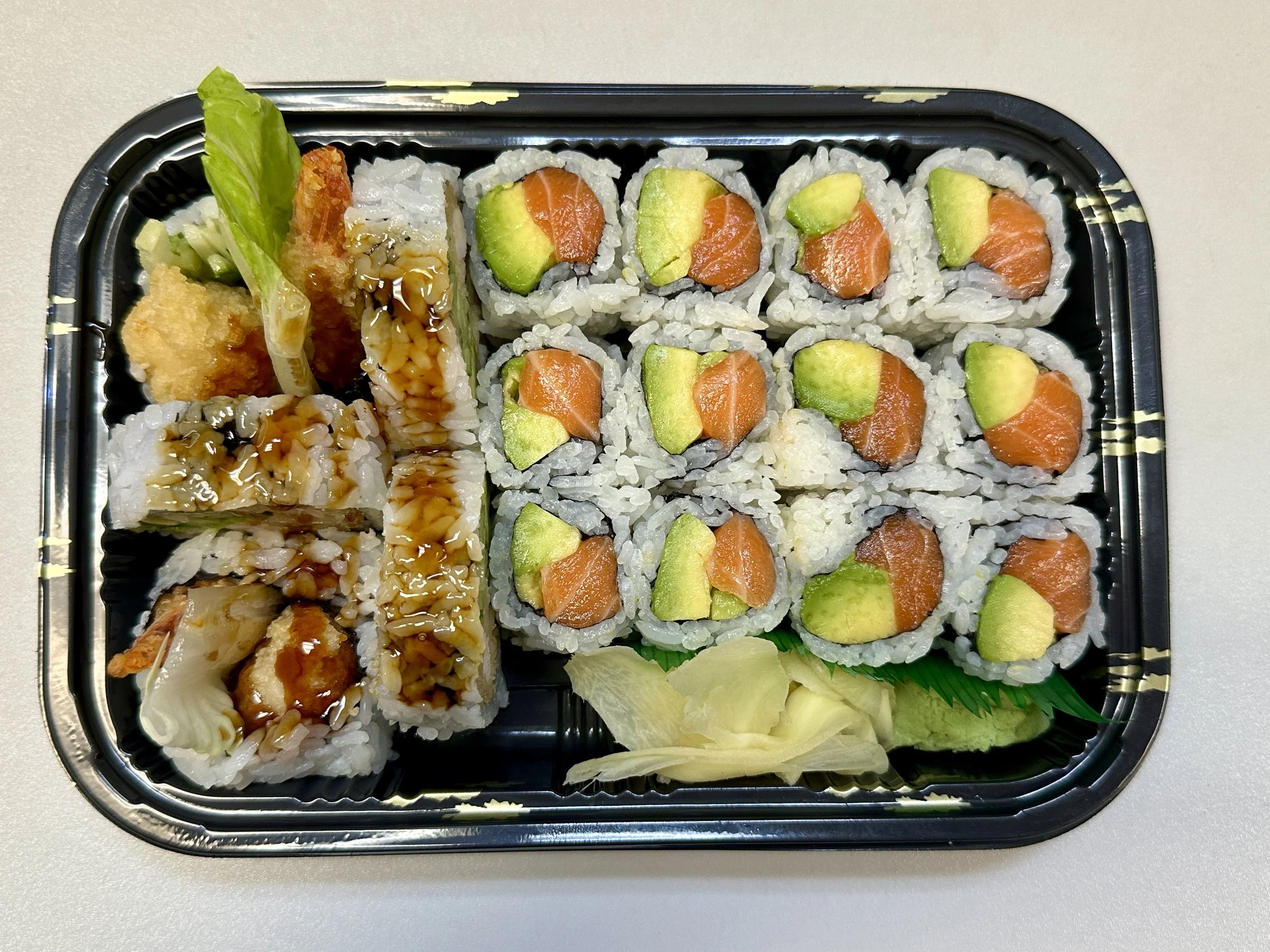 Sushi platter with various sushi rolls, including salmon and avocado, served with ginger and wasabi.