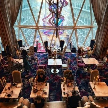 View from a ship deck during sunset, showing calm water and a colorful sky, with the ship's edge and windows illuminated in yellow.