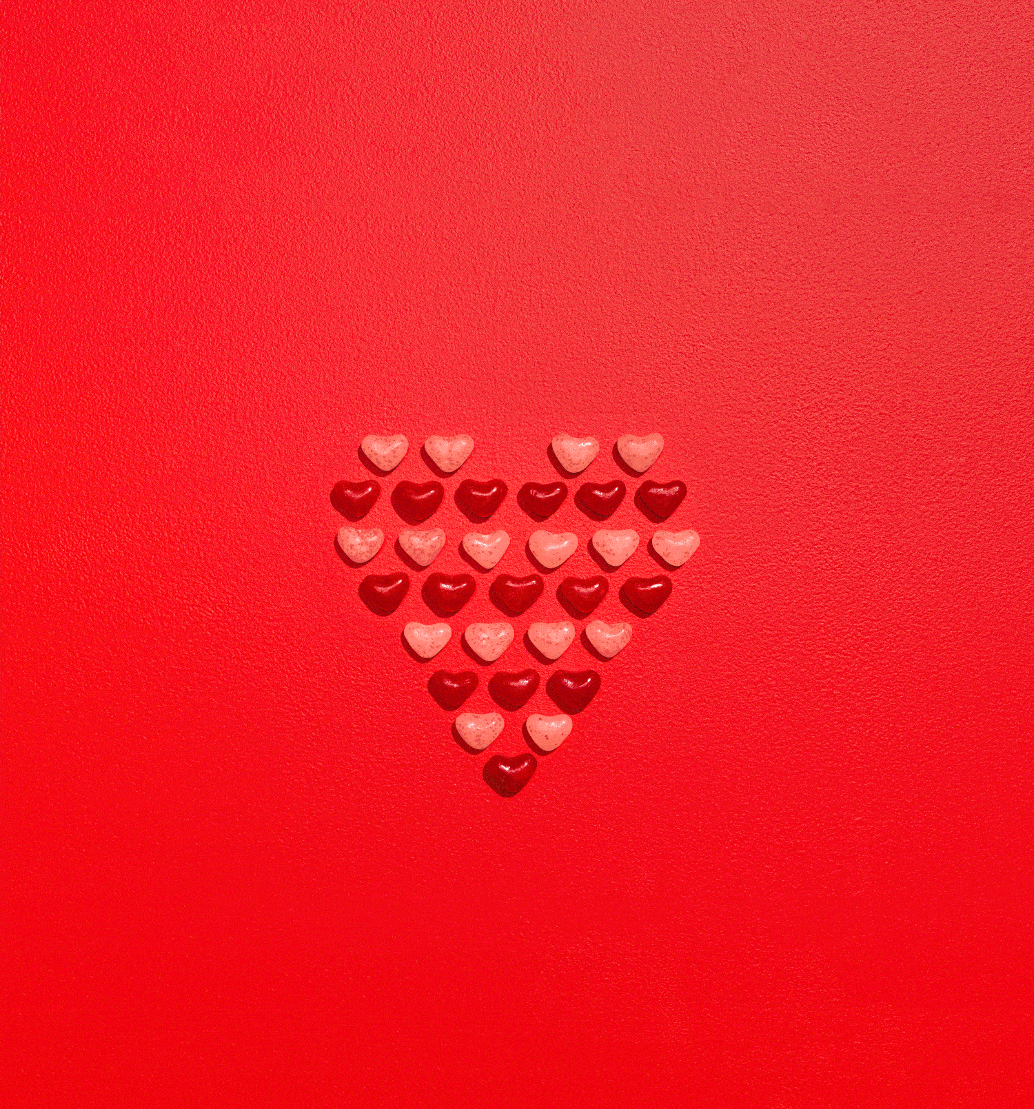 Small red and pink candy hearts arranged in the shape of a heart on a red background.