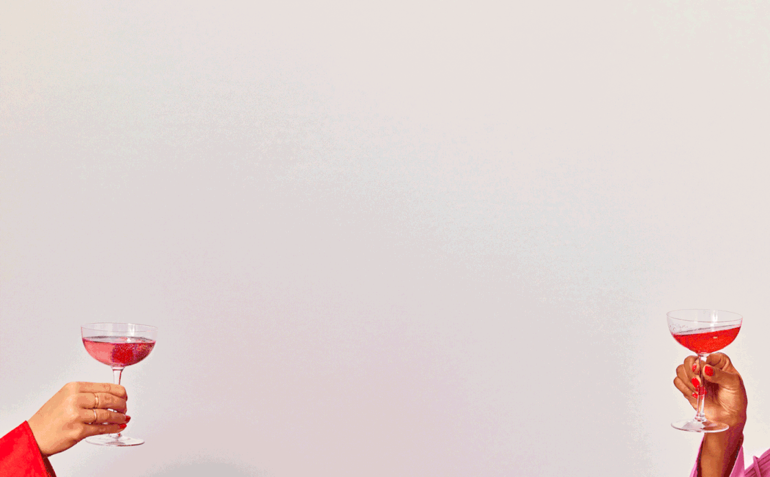 Two hands holding cocktail glasses filled with pink drink, one on each side of the image, against a plain white background.
