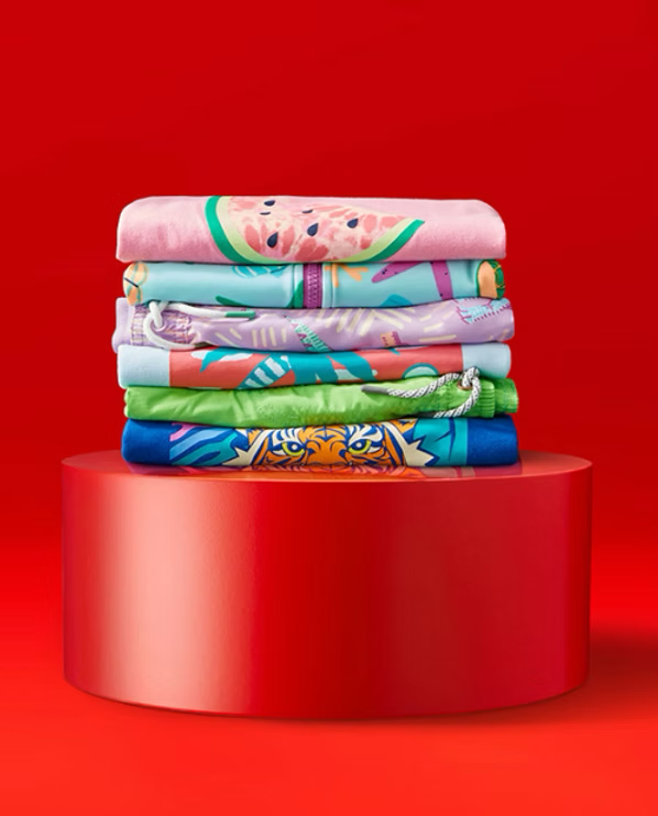Stack of colorful folded hoodies on red cylindrical pedestal against red background.