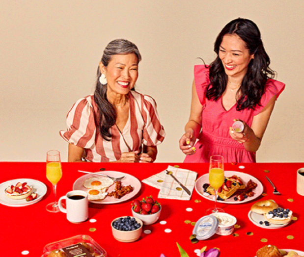 Two women smiling and laughing at a table with breakfast foods, drinks, and strawberries.