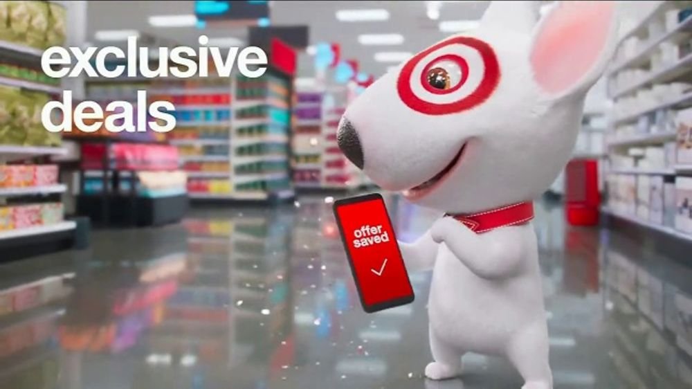 Cartoon mouse character with Target logo eyes holding a phone with a red screen saying 'offer saved' inside a grocery store aisle with shelves of products; text overlay says 'exclusive deals'.