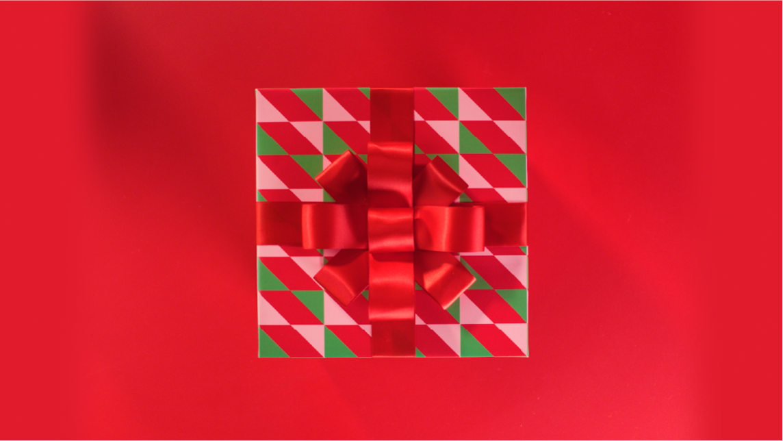 A Christmas gift box wrapped in paper with red, green, and white diagonal stripes, decorated with a big red satin bow, on a red background.