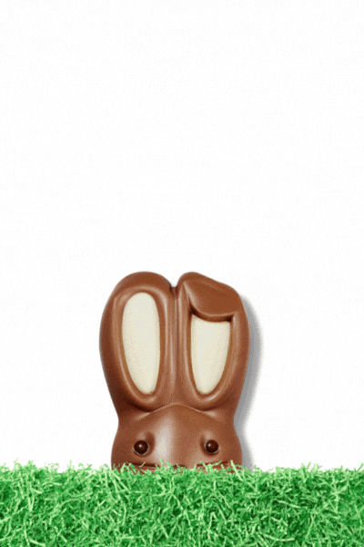Chocolate bunny-shaped candy with white chocolate ears, lying upside down on green artificial grass.