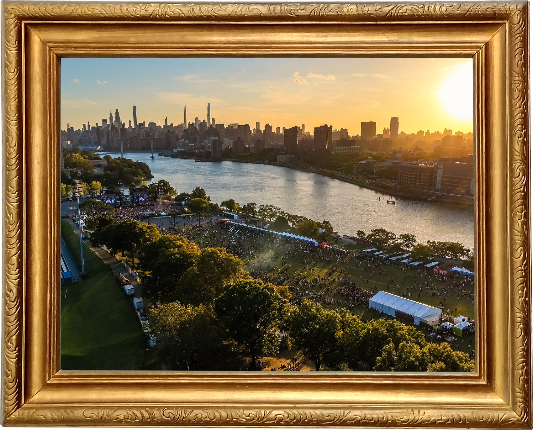A city skyline at sunset seen through a decorative gold picture frame. The skyline features tall buildings and a river in the foreground. Below, a large outdoor concert or event with many people, tents, and trees is visible.