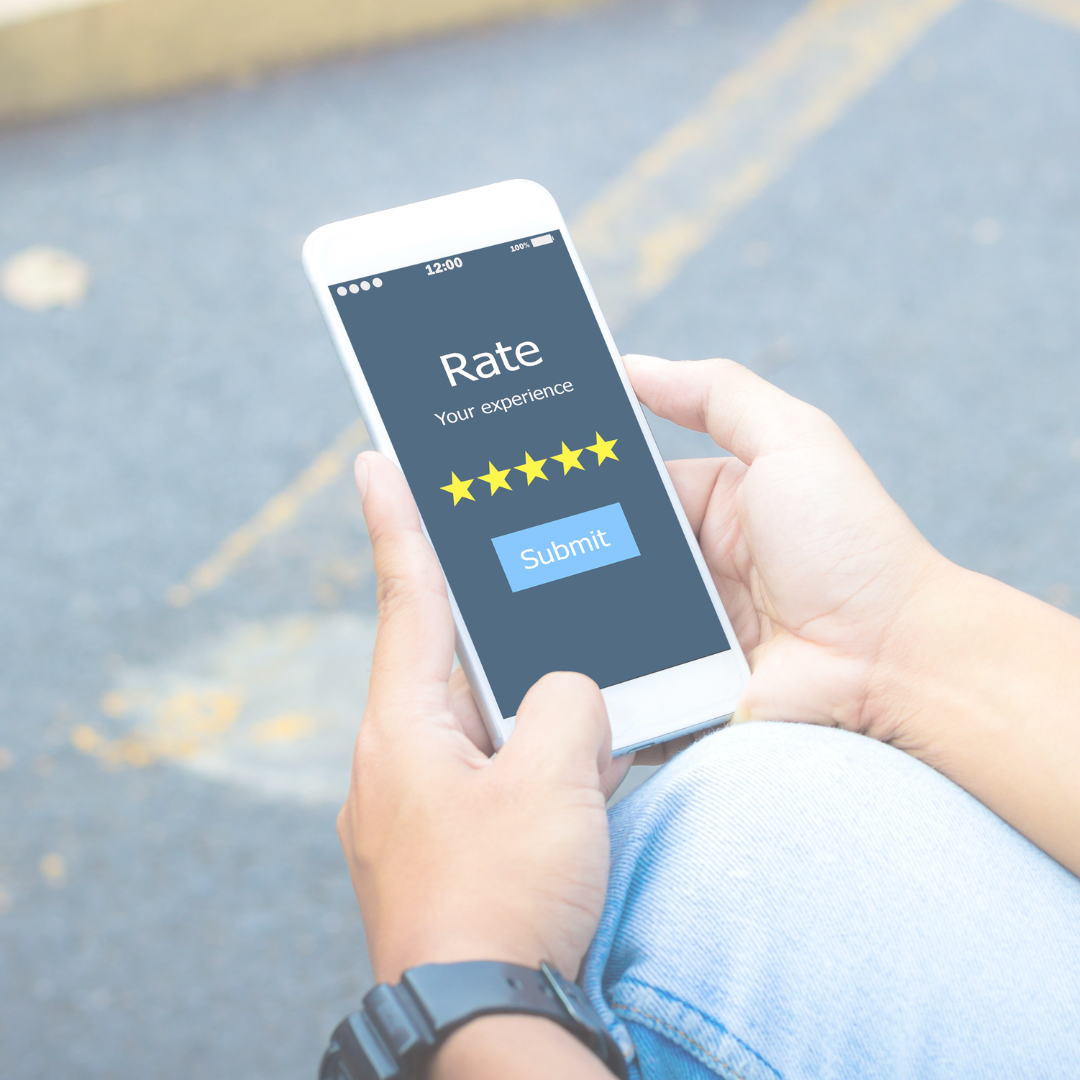 Person holding a smartphone with a screen showing a 5-star rating and a submit button, outdoors on a paved surface with yellow lane markings.