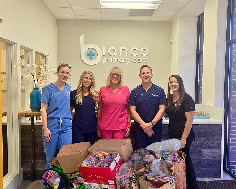 Group of five healthcare professionals standing behind donation boxes filled with candy at Bianco Primary Care, smiling for the photo.