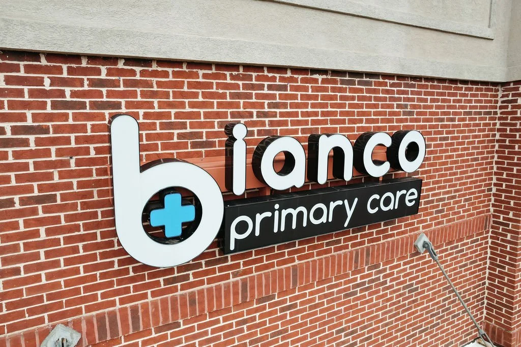 Sign for Bianco Primary Care medical office mounted on a brick wall.