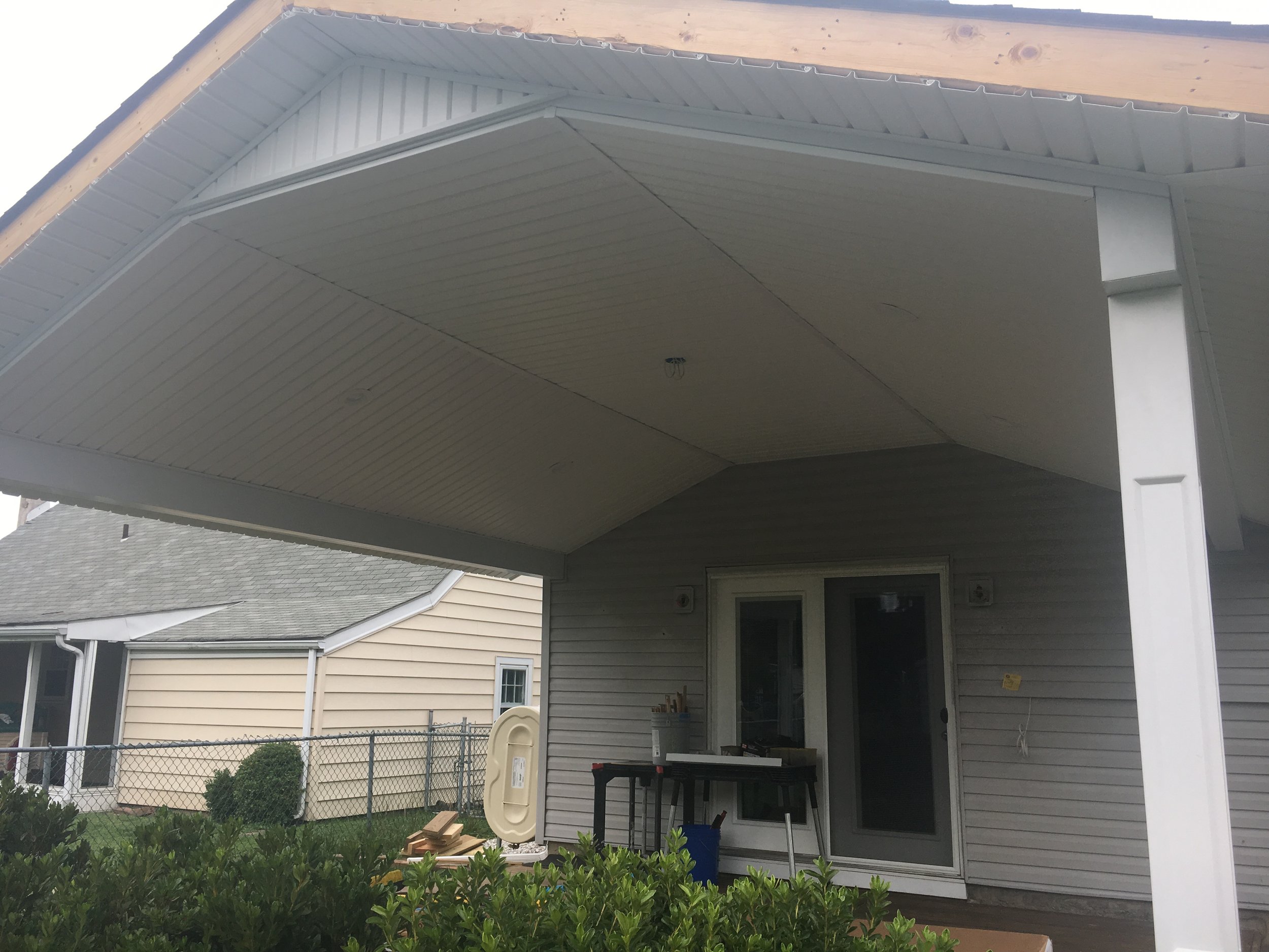 The back porch of a house with a new white ceiling and a partially finished gable roof extension.