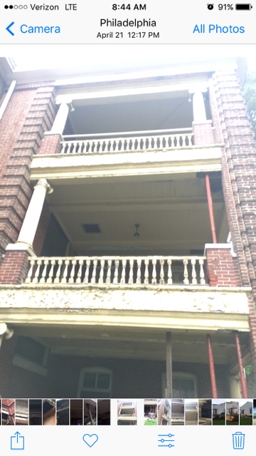 Close-up of a three-story brick building with balconies featuring ornate railings, some with exposed supports and construction equipment.