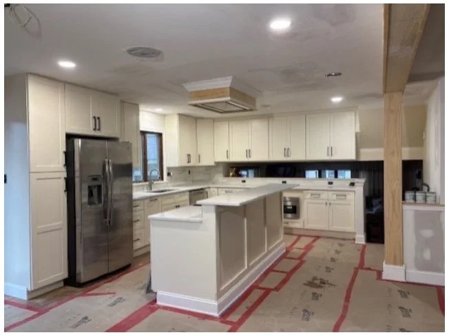 Kitchen with white cabinets, stainless steel refrigerator, and an island with a partially installed ceiling feature.