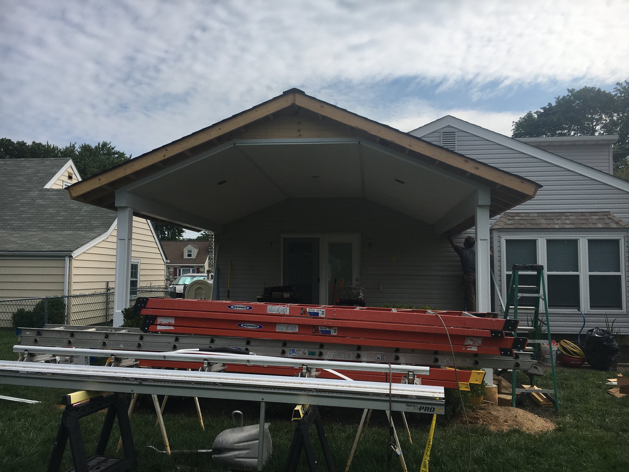 Construction workers building a porch extension with ladders and tools in a residential backyard.