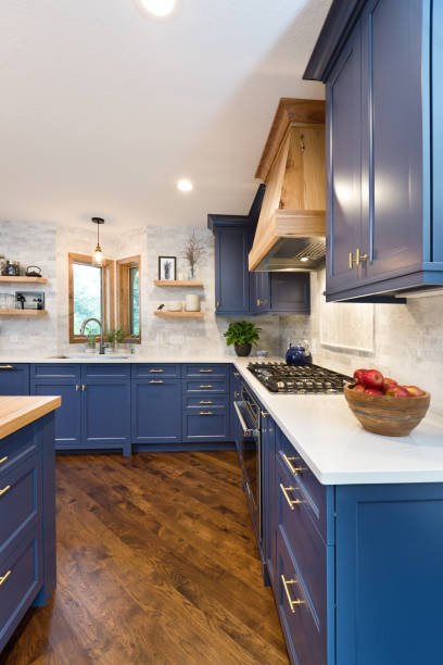 Blue kitchen cabinets with white countertops, wooden flooring, open shelving, and a window with a view outside.