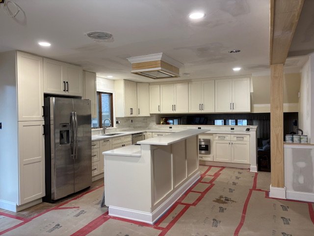 Kitchen with white cabinets, stainless steel refrigerator, and an island with a partially installed ceiling feature.