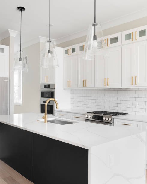 Modern kitchen featuring white cabinets with gold handles, white subway tile backsplash, stainless steel appliances, a white island with a gold faucet, and three hanging pendant lights with glass shades.