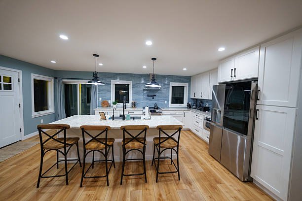 Modern kitchen with white cabinets, stainless steel appliances, hardwood floor, and a large island with five bar stools.