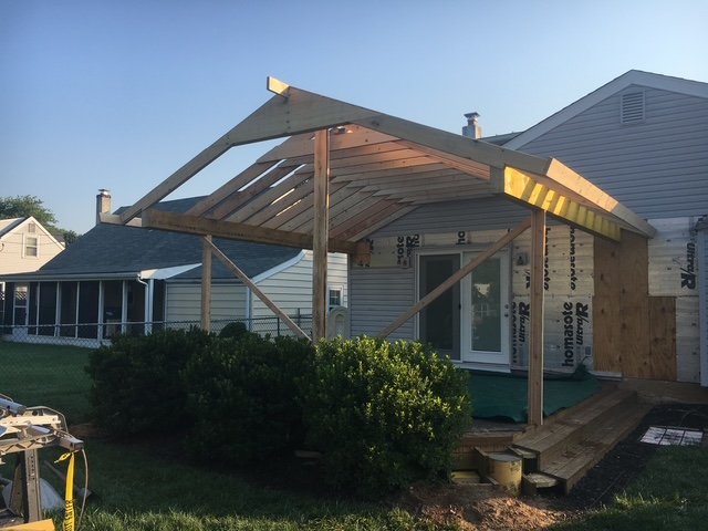 House under construction with wooden framework and a new roof extension, neighboring houses visible in the background.