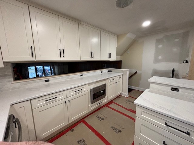 Kitchen under renovation with white cabinets, a marble countertop, a built-in microwave, and no appliances or furnishings installed yet.