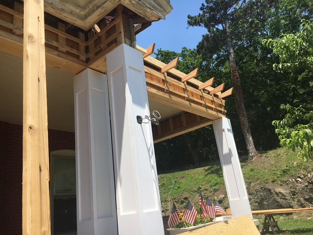 Wooden deck under construction with white panels and American flags displayed below on a grassy area.