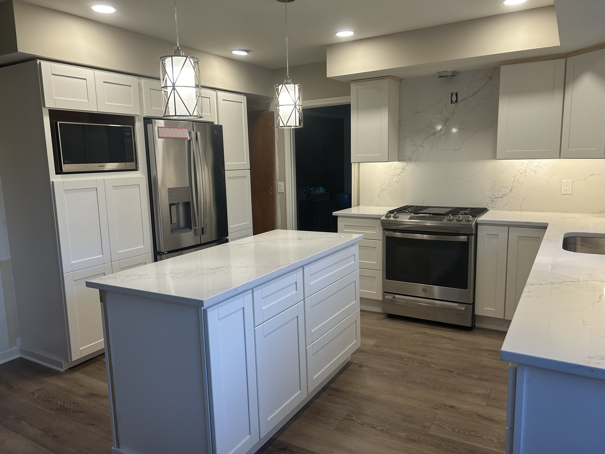 Modern kitchen with white cabinets, marble countertops, stainless steel appliances, and wooden floor.