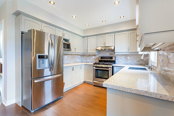 Modern kitchen with stainless steel refrigerator, stove, built-in microwave, white cabinets, granite countertops, and wood flooring.