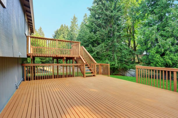 Large wooden outdoor deck with stairs and railings overlooking a backyard with green trees.