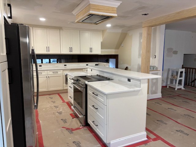 Modern kitchen with white cabinets, stainless steel refrigerator, and an island with a stove, under construction with protective floor covering.