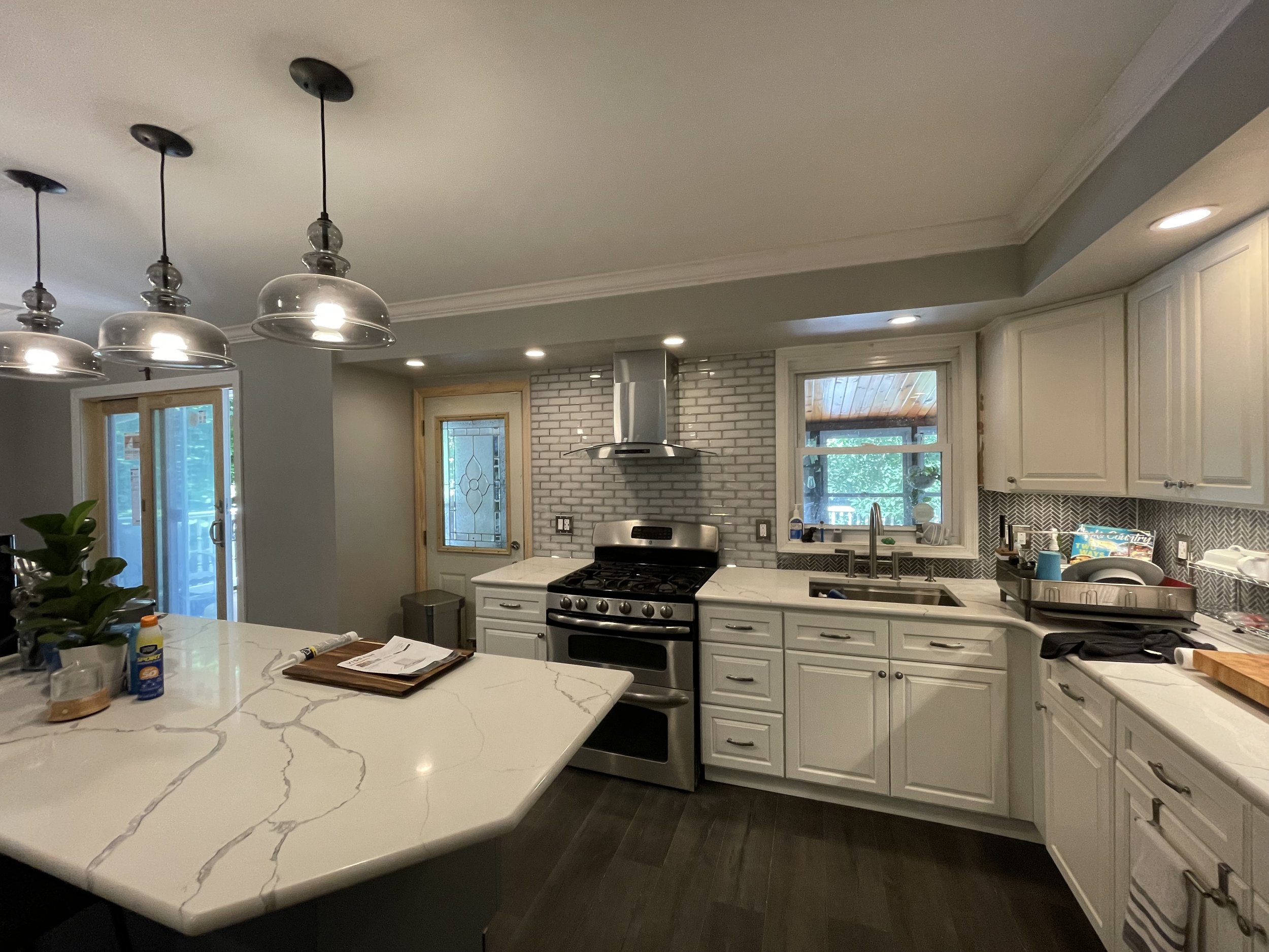 Kitchen with white cabinets, marble countertop island, stainless steel stove, brick backsplash, and windows with trees visible outside.