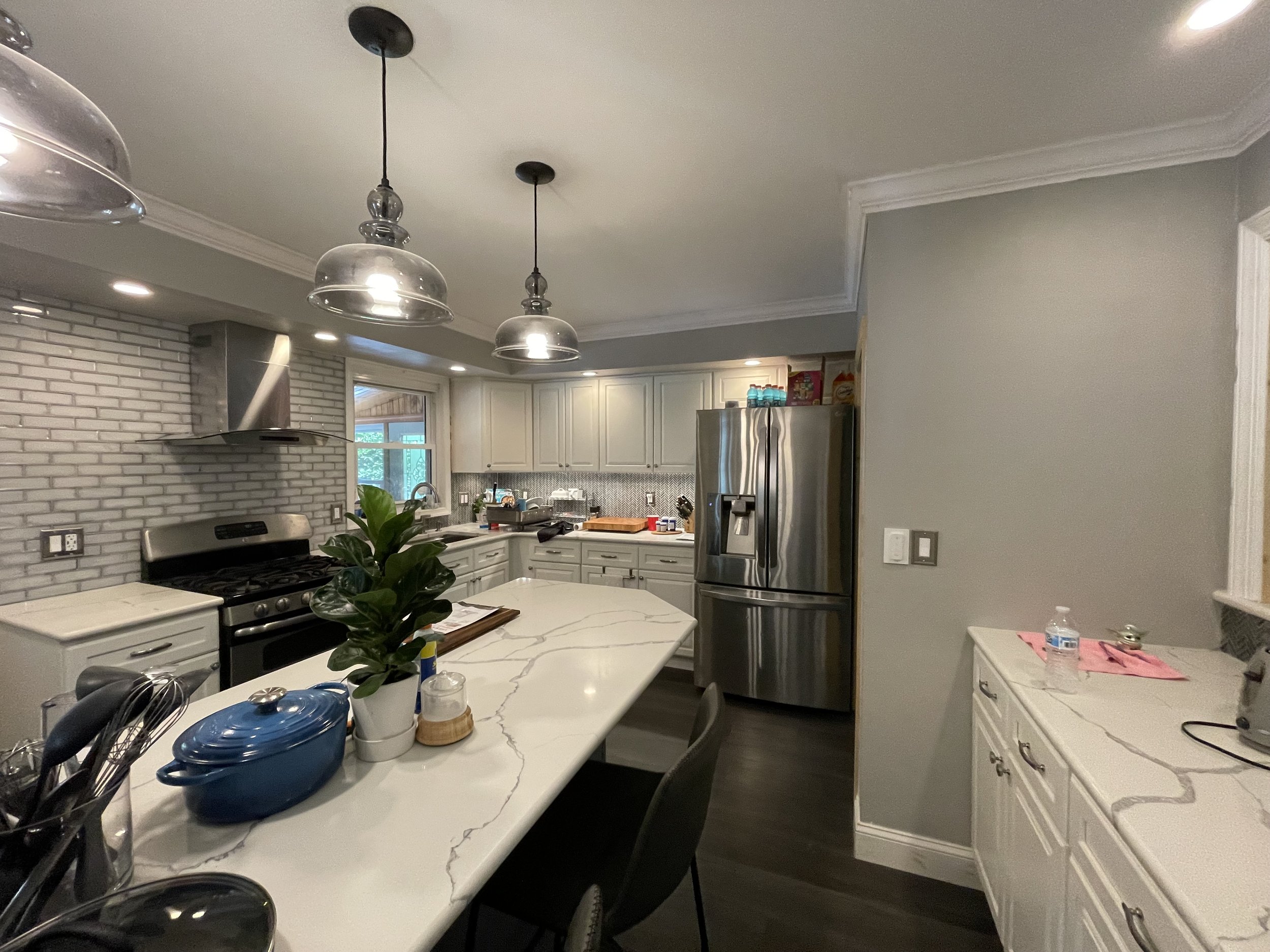 Modern kitchen with white cabinets, a marble island, stainless steel appliances, pendant lighting, and a gray accent wall.