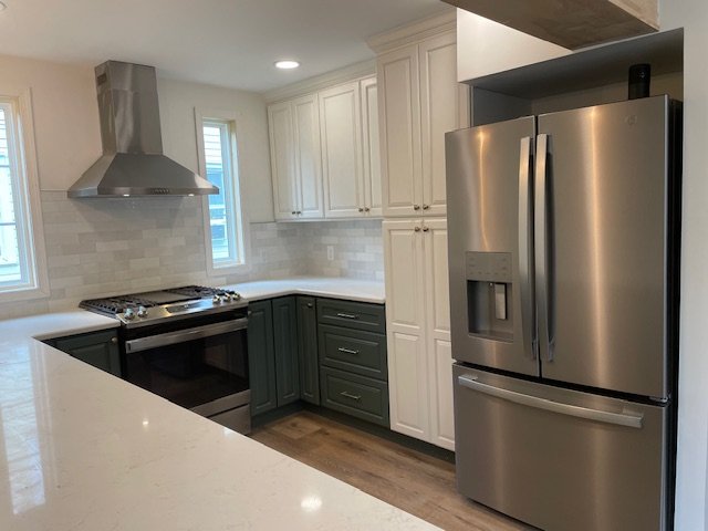 Modern kitchen with white upper cabinets, dark lower cabinets, stainless steel appliances, a stainless steel refrigerator, and a stainless steel stove with a range hood.