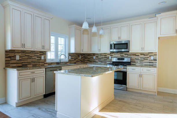 Kitchen with white cabinets, granite countertop island, wood-look tile flooring, stainless steel appliances, and a colorful tile backsplash.
