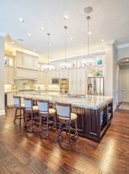 Modern kitchen with white cabinetry, stainless steel refrigerator, large island with granite countertop, four bar stools, hardwood flooring, pendant lighting, and built-in appliances.