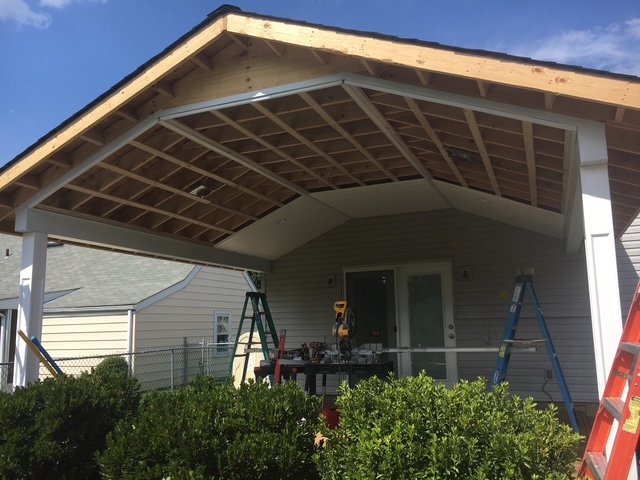 House with an unfinished porch roof under construction, with ladders and tools present.