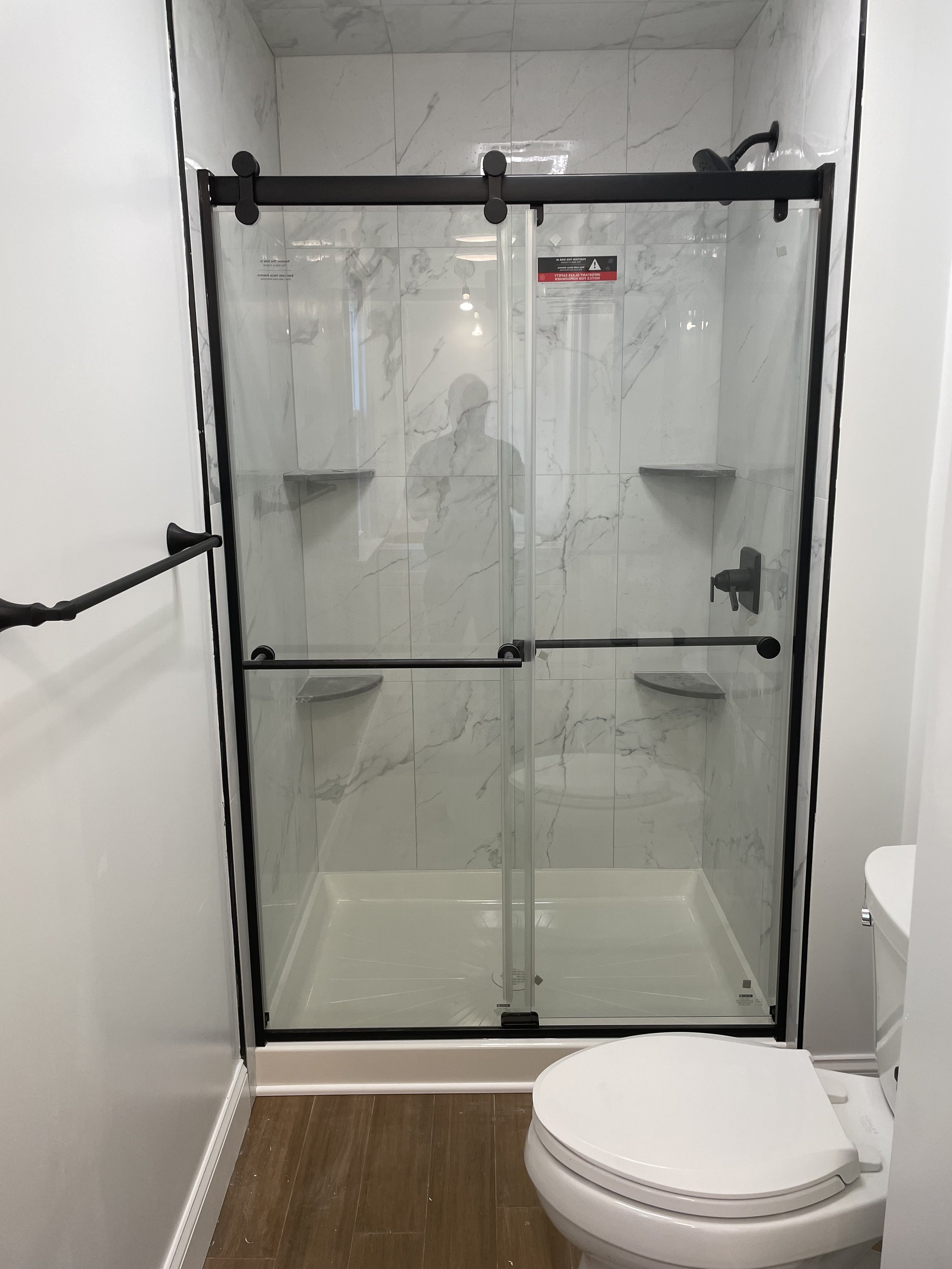 Bathroom with a glass shower enclosure, white marble tiled walls, wooden floor, and a white toilet.