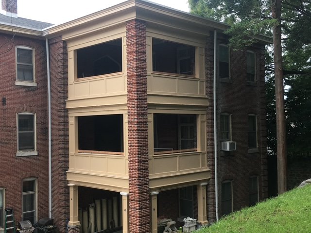 Three-story screened-in porch addition on the back of a brick apartment building under construction.