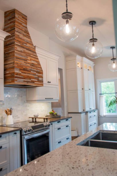 Modern kitchen with white cabinets, a granite countertop, a stove, a brick vent hood, pendant lights, and a window with a view of greenery.